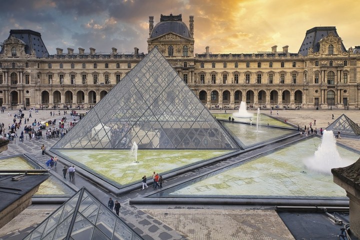 Glass pyramid and historic building at Louvre Museum courtyard with people and fountains.