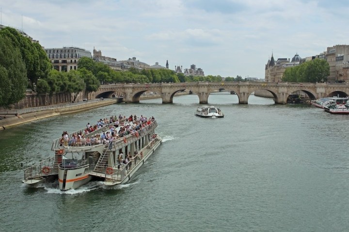 A boat with passengers sails on a river toward a bridge in a cityscape.