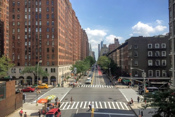 City street intersection with tall buildings, people, and vehicles on a sunny day.