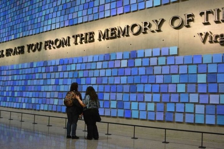 Two people view a memorial wall with quote and blue tiles in a museum.