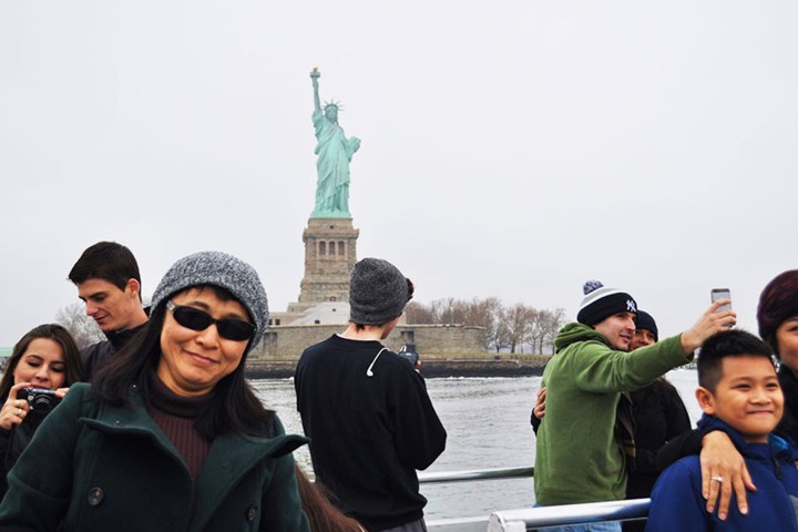 Tourists on a boat taking photos with the Statue of Liberty in the background.