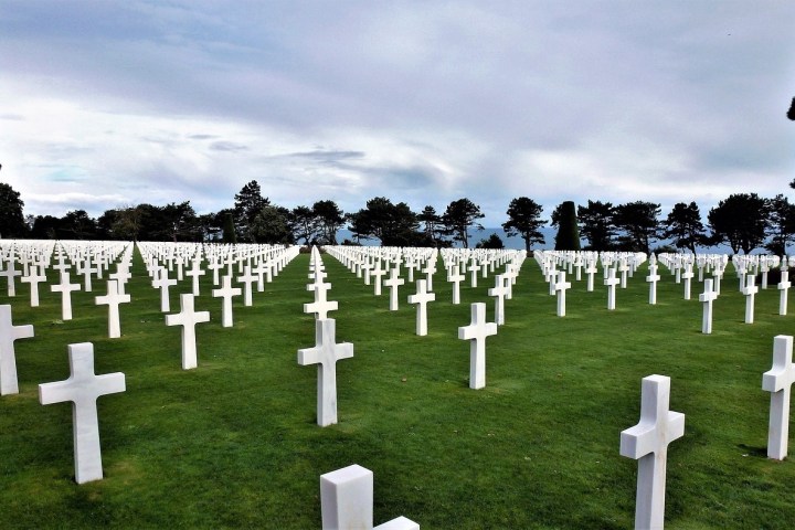 Rows of white crosses on a green lawn under a cloudy sky, resembling cemetery
