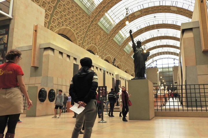 People inside a museum with a statue of Liberty replica and arched ceiling.