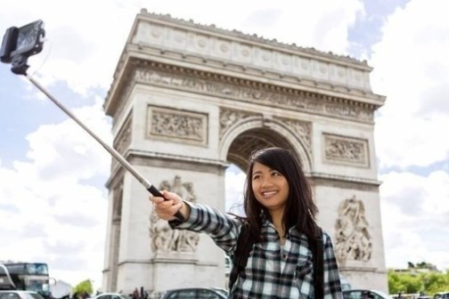 Woman taking selfie with a selfie stick in front of the Arc de Triomphe in Paris.