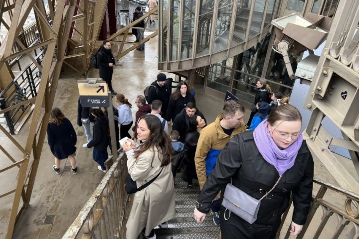 People walking on the Eiffel Tower stairs, crowded area, metal structure visible.