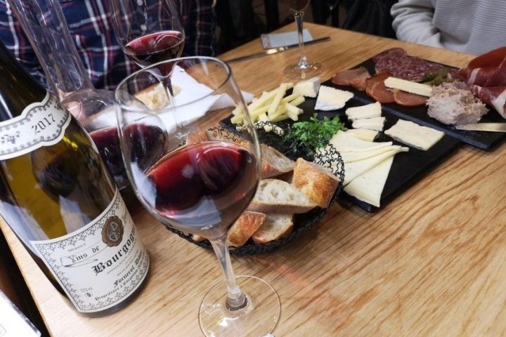 Table with wine, cheese, bread, and charcuterie on wooden surface.