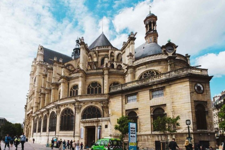 Historic church with towers and arches under a blue sky, people walking nearby.