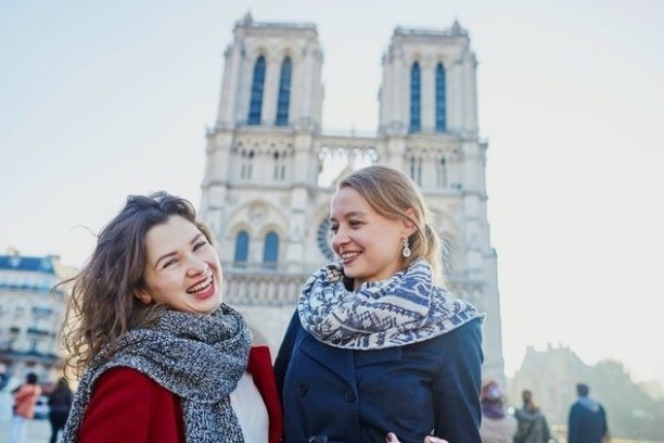 Two women smiling in front of Notre Dame Cathedral on a sunny day.