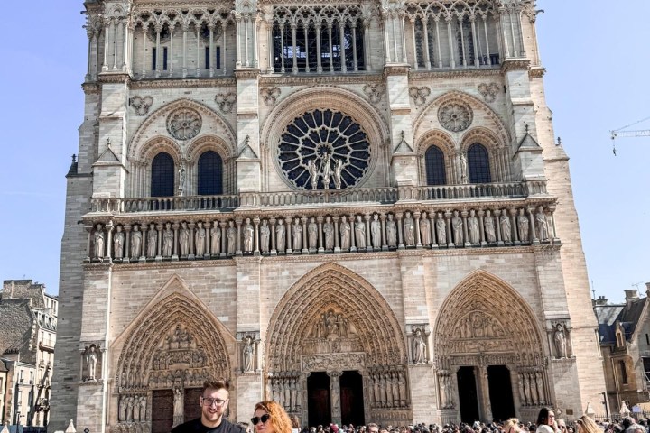 A couple posing in front of Notre Dame Cathedral with a crowd of tourists.