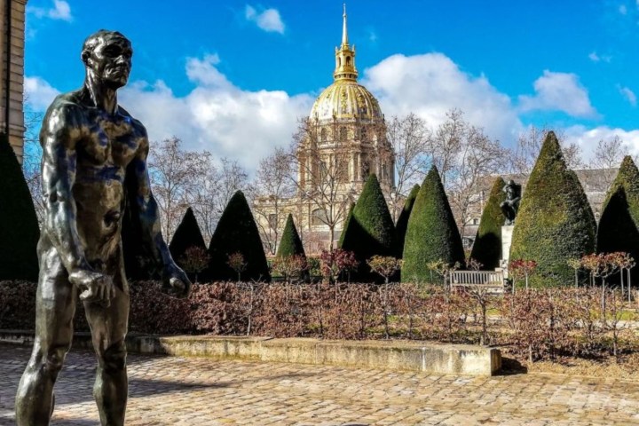 Bronze statue in garden with dome and trimmed trees under a blue sky.