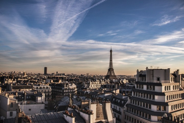 Rooftop view of Paris with the Eiffel Tower under a blue sky with scattered clouds.