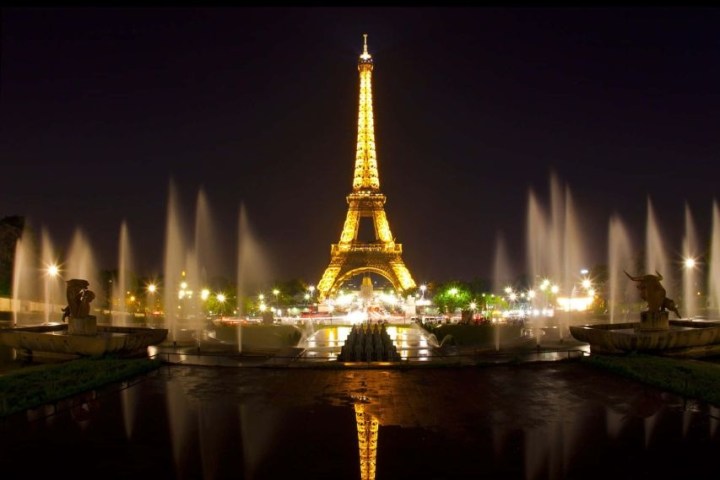 Illuminated Eiffel Tower at night with fountain reflections in foreground.
