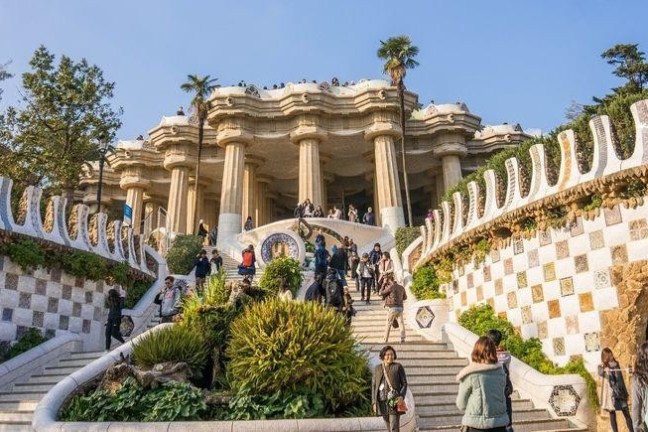 People walking on stairs in front of an ornate building with columns and decorative patterns.