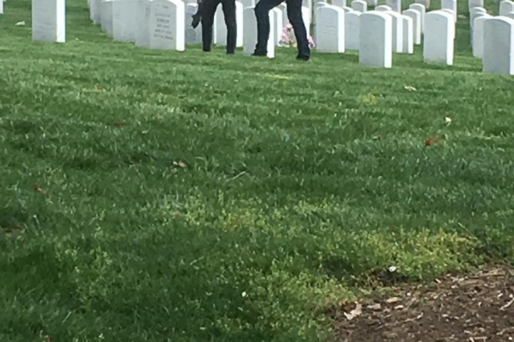 Two people standing among rows of white tombstones in a cemetery.