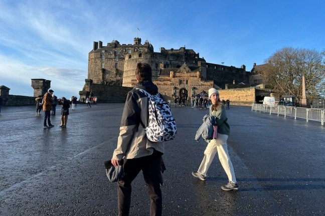 People walking toward a large historical castle under a clear blue sky.
