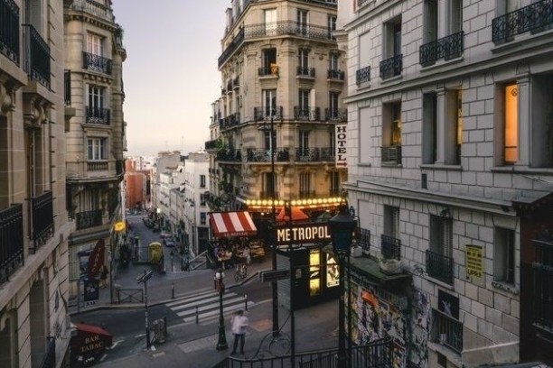 Narrow European street with cafes, buildings, and Metropol sign at dusk.