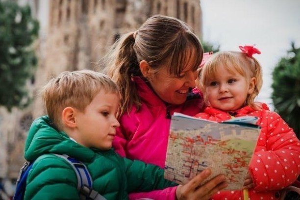 Woman with two kids looking at a map. They wear colorful jackets outside near a historic building.