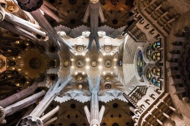 Intricate ceiling of a cathedral with columns and colorful stained glass windows.