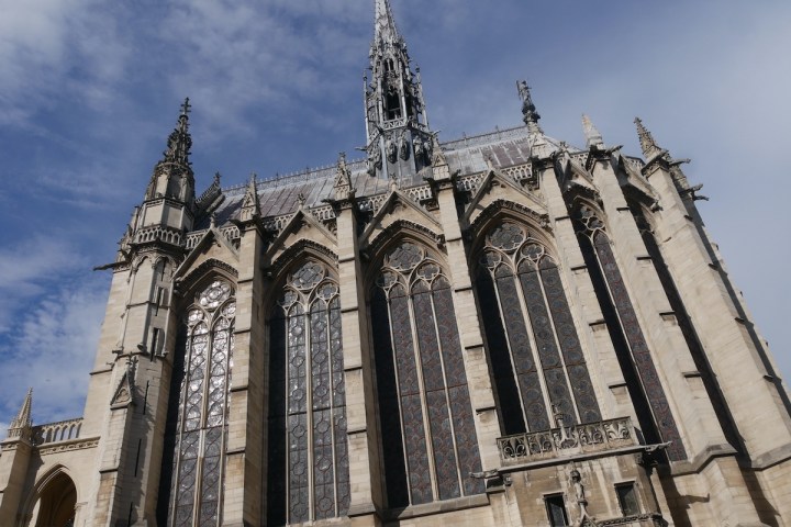 Gothic cathedral facade with large stained glass windows and intricate spires under a blue sky.