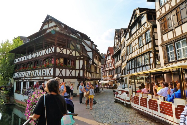 Tourists and a tram in a picturesque street with half-timbered houses.