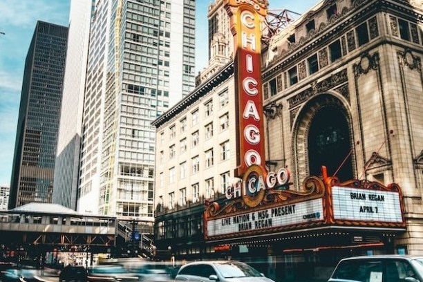 Chicago theater sign with cars passing in busy urban street, tall buildings in background.