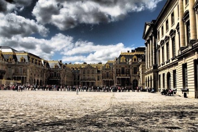 Crowd at a historic palace with ornate architecture under a cloudy sky.