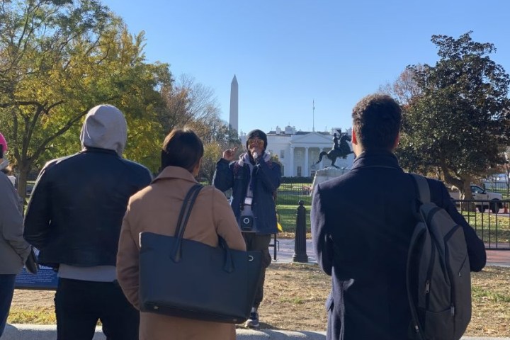 Person giving a tour to a group near the White House and Washington Monument on a sunny day.
