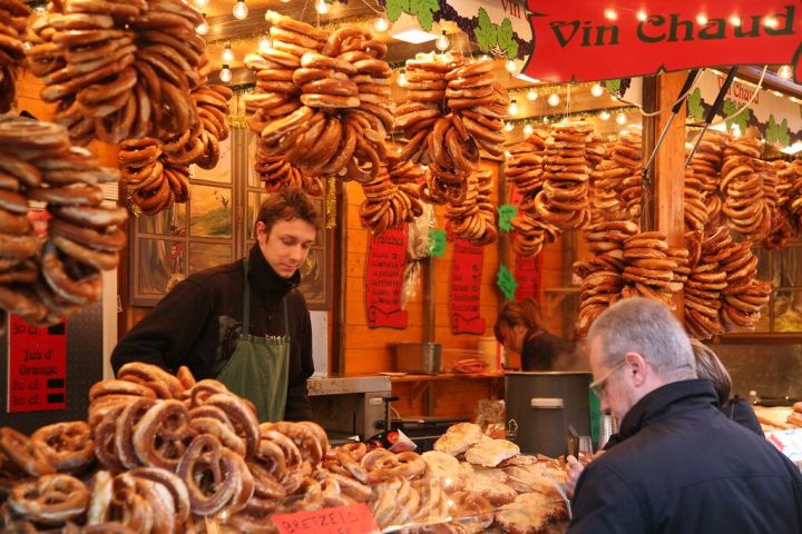 Market stall with pretzels hanging, man selling under string lights.