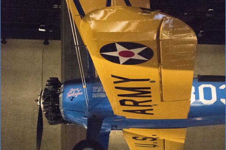 Yellow-winged vintage biplane with U.S. Army markings on display indoors.