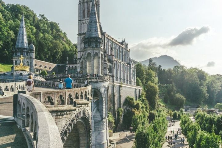 Gothic cathedral on a hill with trees and people walking on a sunny day.