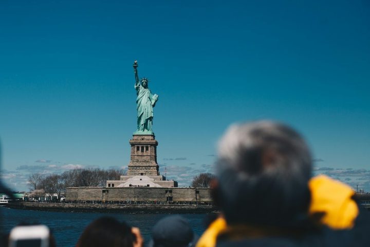 Statue of Liberty with tourists taking photos, clear blue sky in the background.