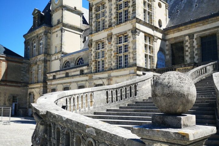 Historic stone building with ornate stairs and tower under blue sky.