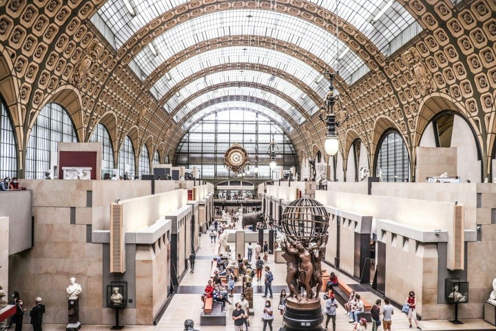 Interior of a grand museum hall with arched glass ceiling and sculpture centerpiece.