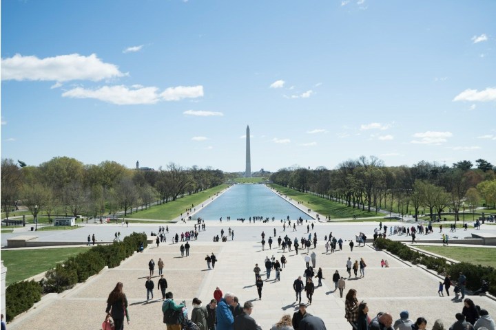 People walking near the Lincoln Memorial Reflecting Pool with the Washington Monument in view on a sunny day.