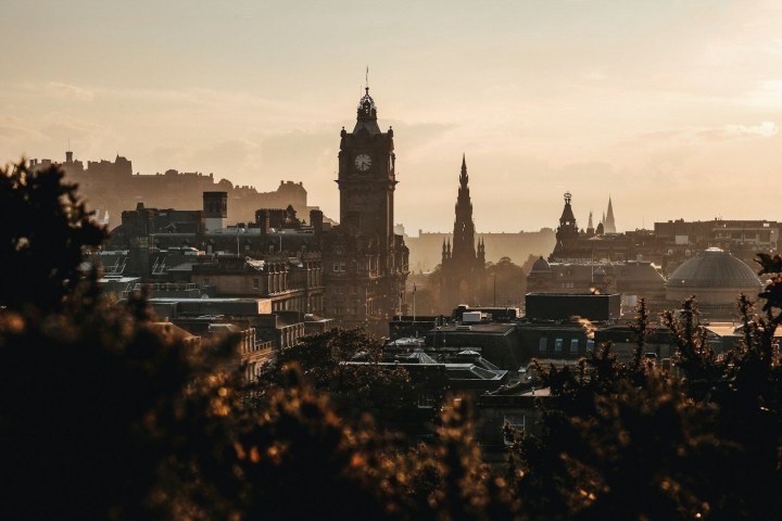 City skyline at sunset with a clock tower and spires silhouetted against orange sky.