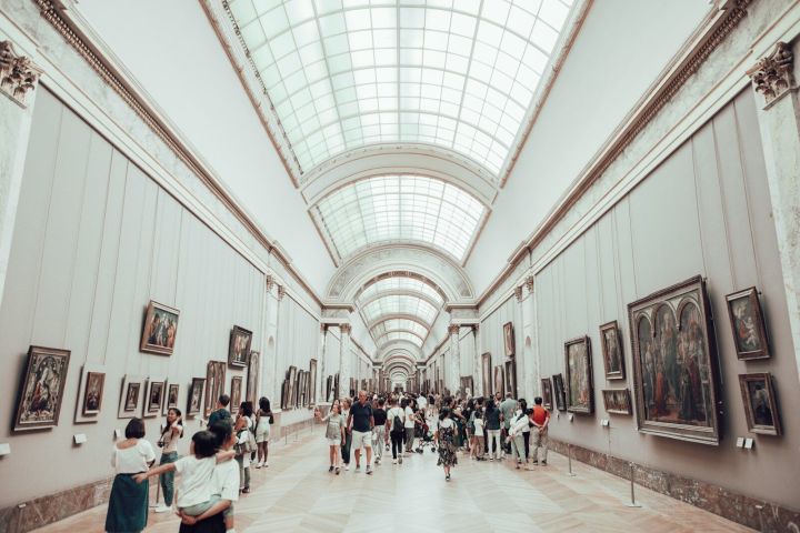 People walking in a large, brightly lit art gallery with paintings on the walls.