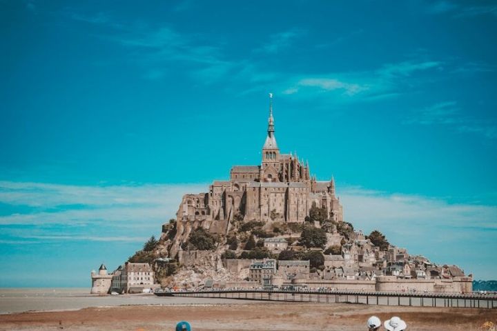 Tourists view Mont Saint-Michel under a blue sky on a sunny day.