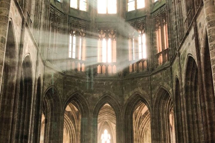 Sunlight streams into a cathedral through tall, arched stained glass windows.