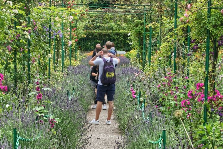 People walking through a vibrant garden with flowers and green arches.