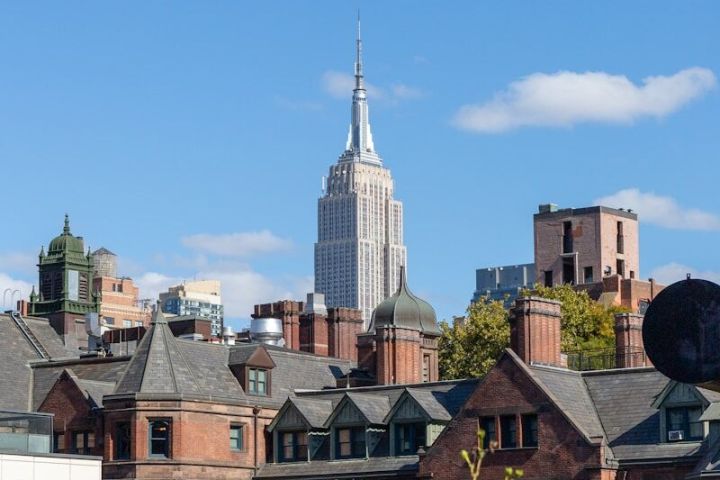 Empire State Building behind historic brownstone buildings with a clear blue sky.