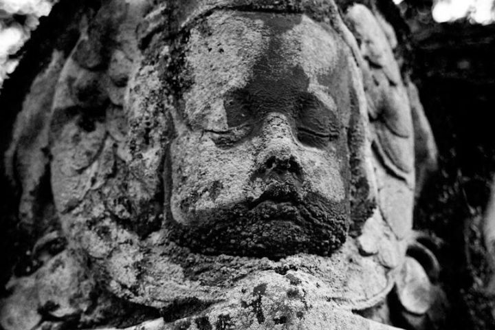 Weathered stone cherub statue in black and white, partially covered in moss.