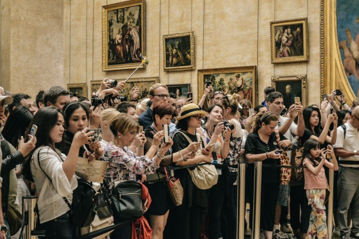 Crowd of people taking photos in a gallery with paintings on the walls.
