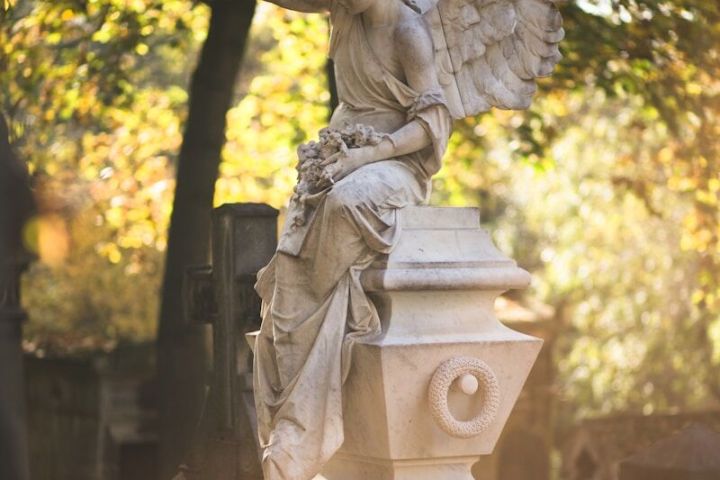 Stone angel statue with wings and flowers in a sunlit cemetery.