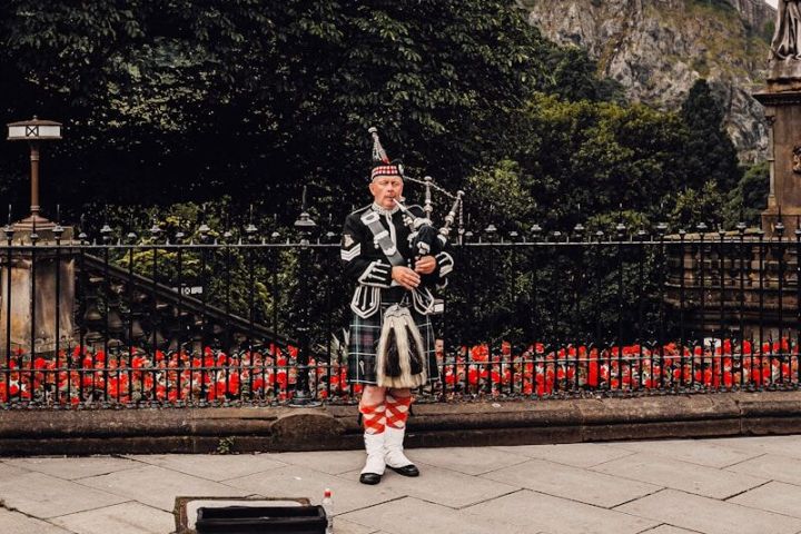 Bagpiper in traditional attire plays on a city street with a castle in the background.