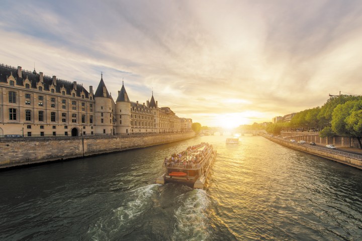 Boat cruising on a river with a sunset and historic building in the background.