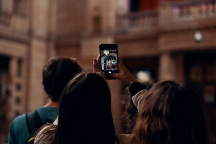 Person takes photo with phone in ornate indoor setting, others in background.