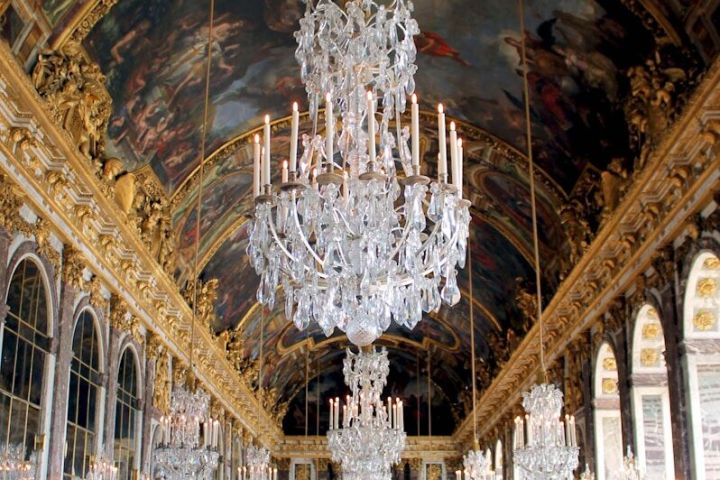 Ornate hall with chandeliers, mirrored walls, and painted ceiling.