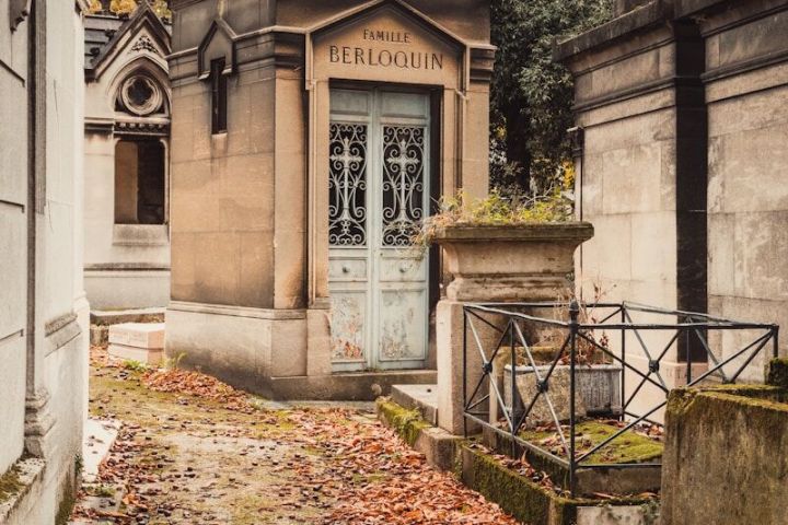 Pathway in a cemetery with tombs and fallen leaves, labeled 'Famille Berloquin' on one tomb.