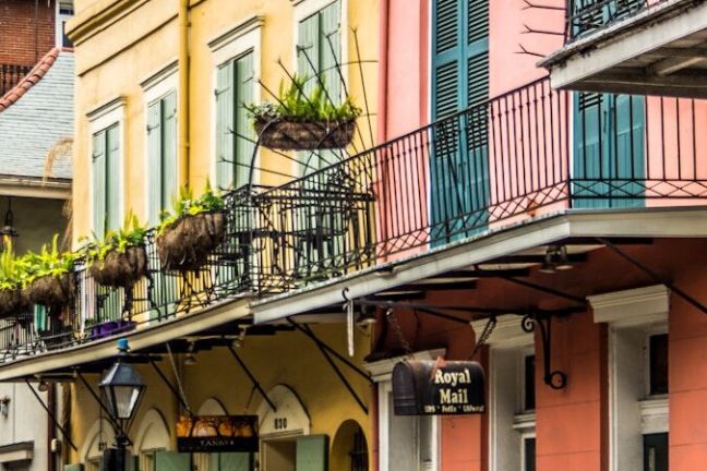 A man walks past colorful buildings with balconies on a street.
