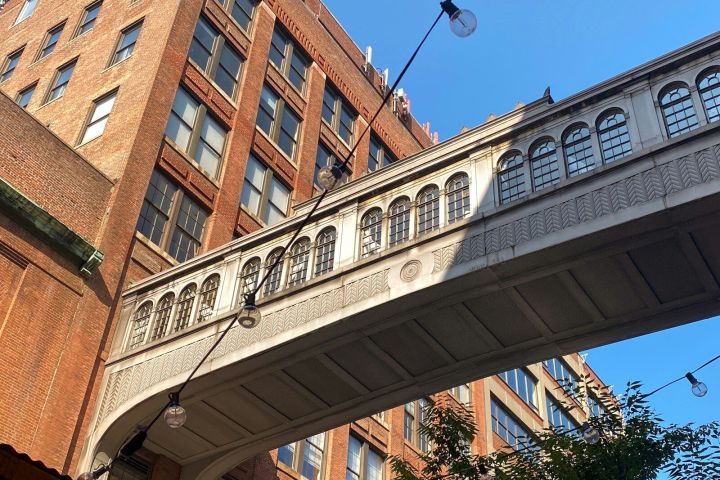 White bridge connecting two brick buildings with string lights in the foreground.